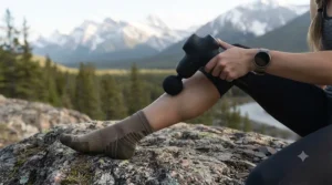 Athlete using a mini massage gun for recovery after outdoor hiking.