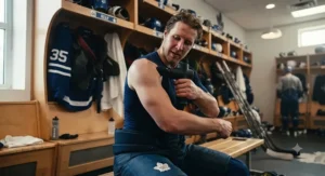 A hockey goalie applying a massage gun to target tight shoulders and upper back
